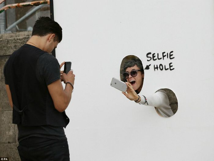 Person taking selfie through selfie hole at Banksy's Dismaland